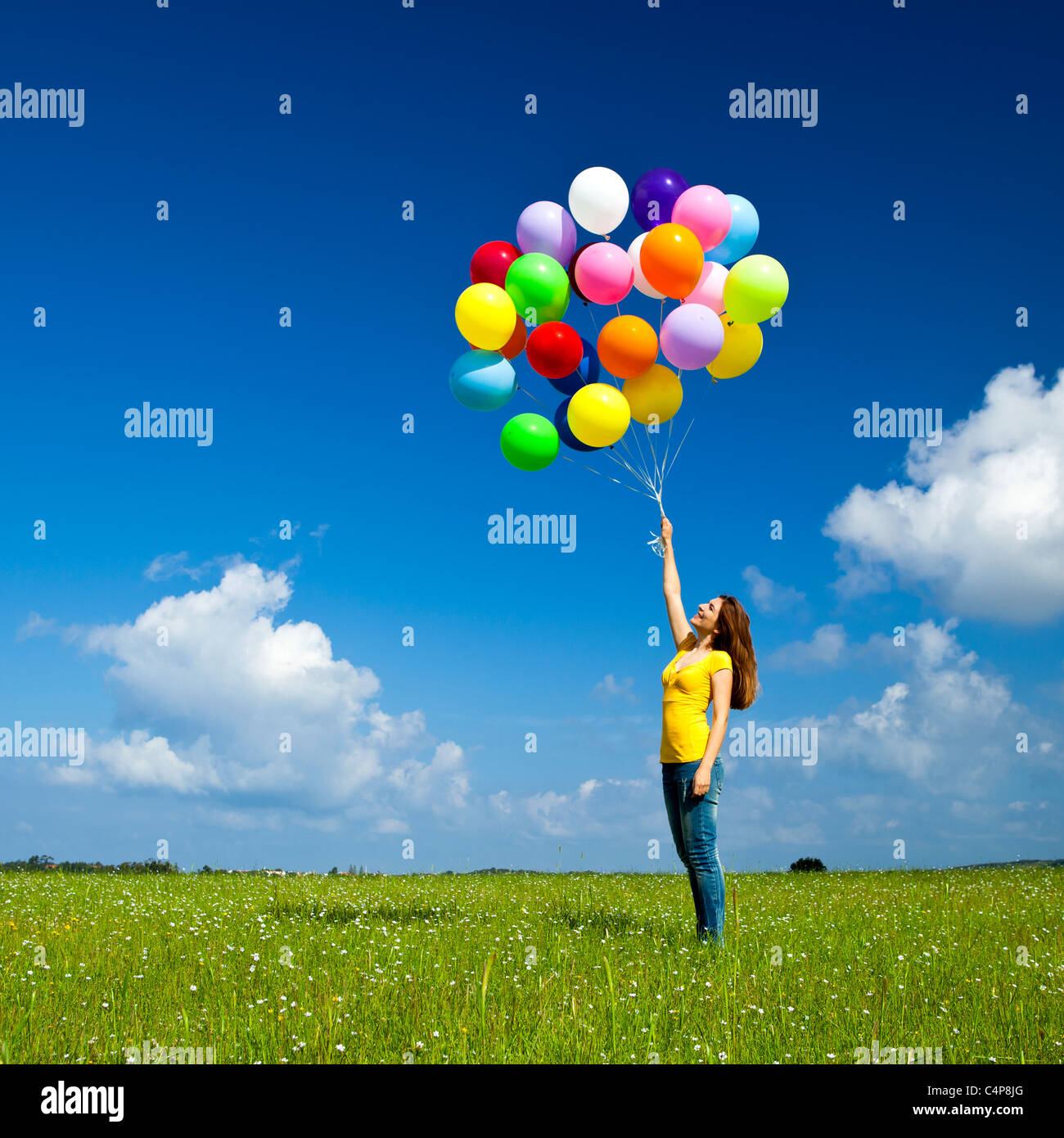 Mujer joven feliz con globos de colores en una pradera verde Foto de stock