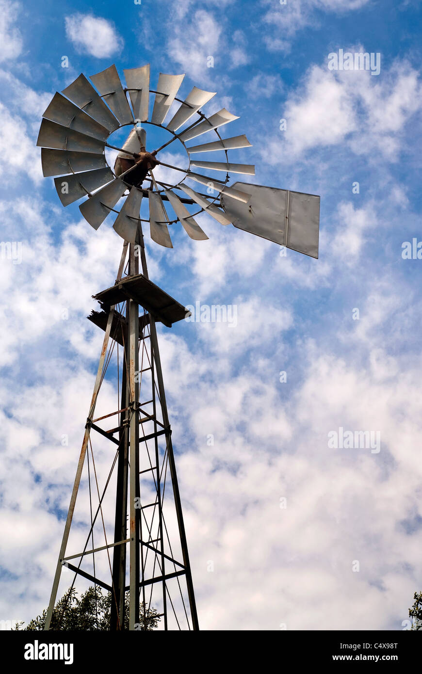Un viejo molino de viento de metal contra un nublado cielo azul. Foto de stock