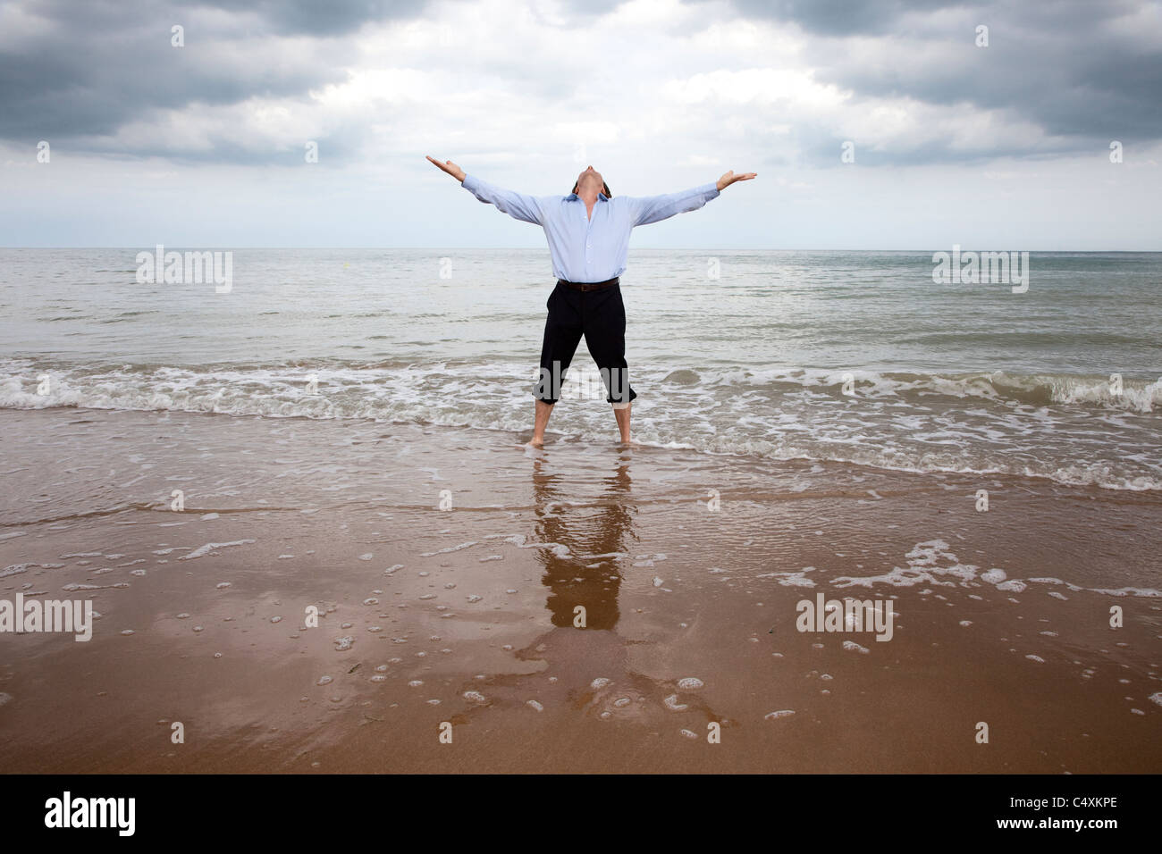 Completamente vestida hombre de pie en el mar con los brazos mirando al cielo. Foto de stock