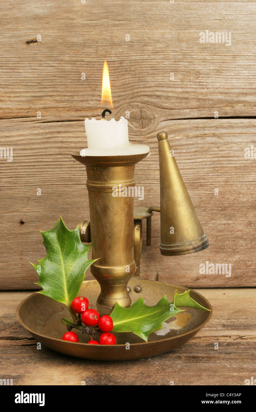 Candelabro de latón con el acebo y velas encendidas contra la madera vieja Foto de stock