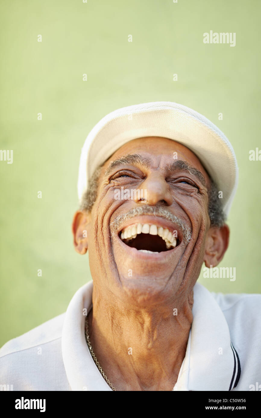 Retrato del hombre hispano senior con sombrero blanco mirando hacia arriba contra la pared verde y sonriente. De forma vertical, espacio de copia Foto de stock
