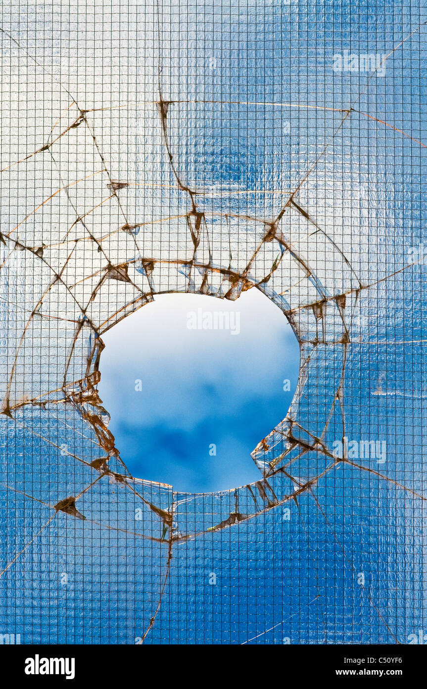 Vidrio roto, agrietado con el agujero en el cielo azul. Foto de stock