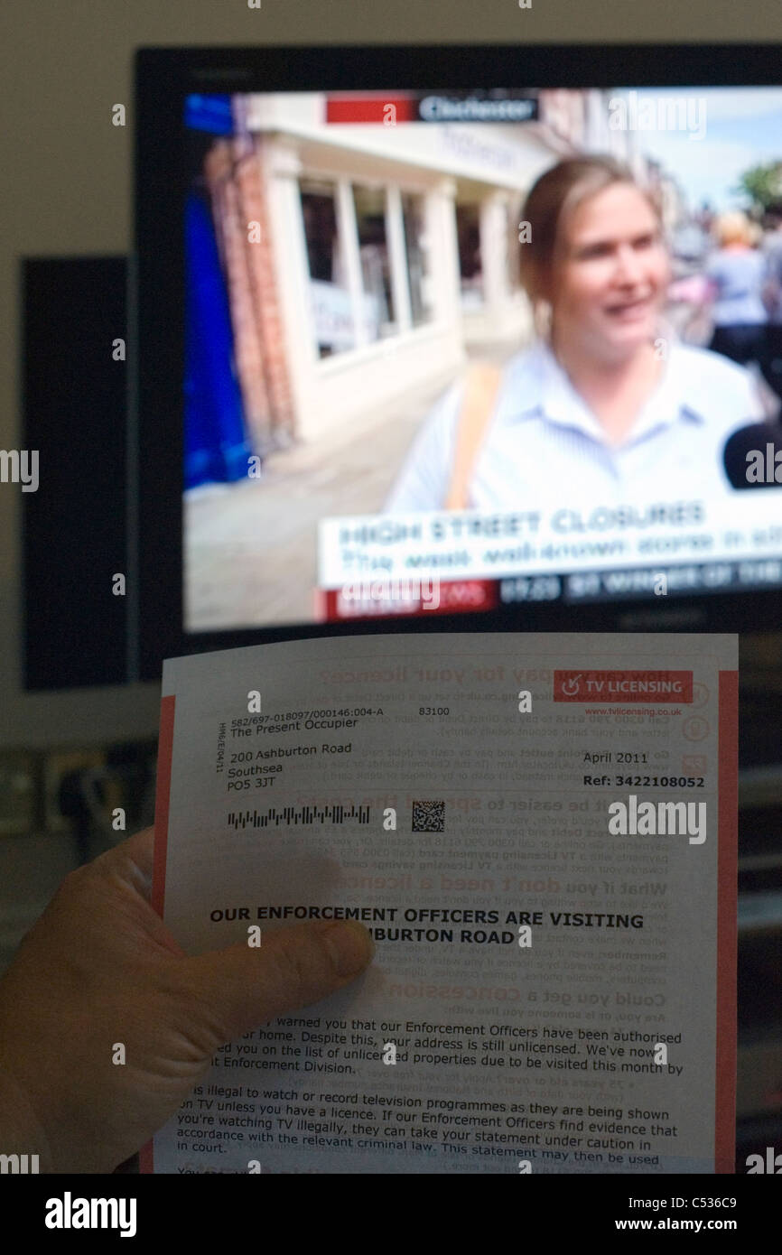 Hombre sujetando carta de advertencia de la visita de autoridades de licencias de televisión de la bbc que muestra en segundo plano. Foto de stock