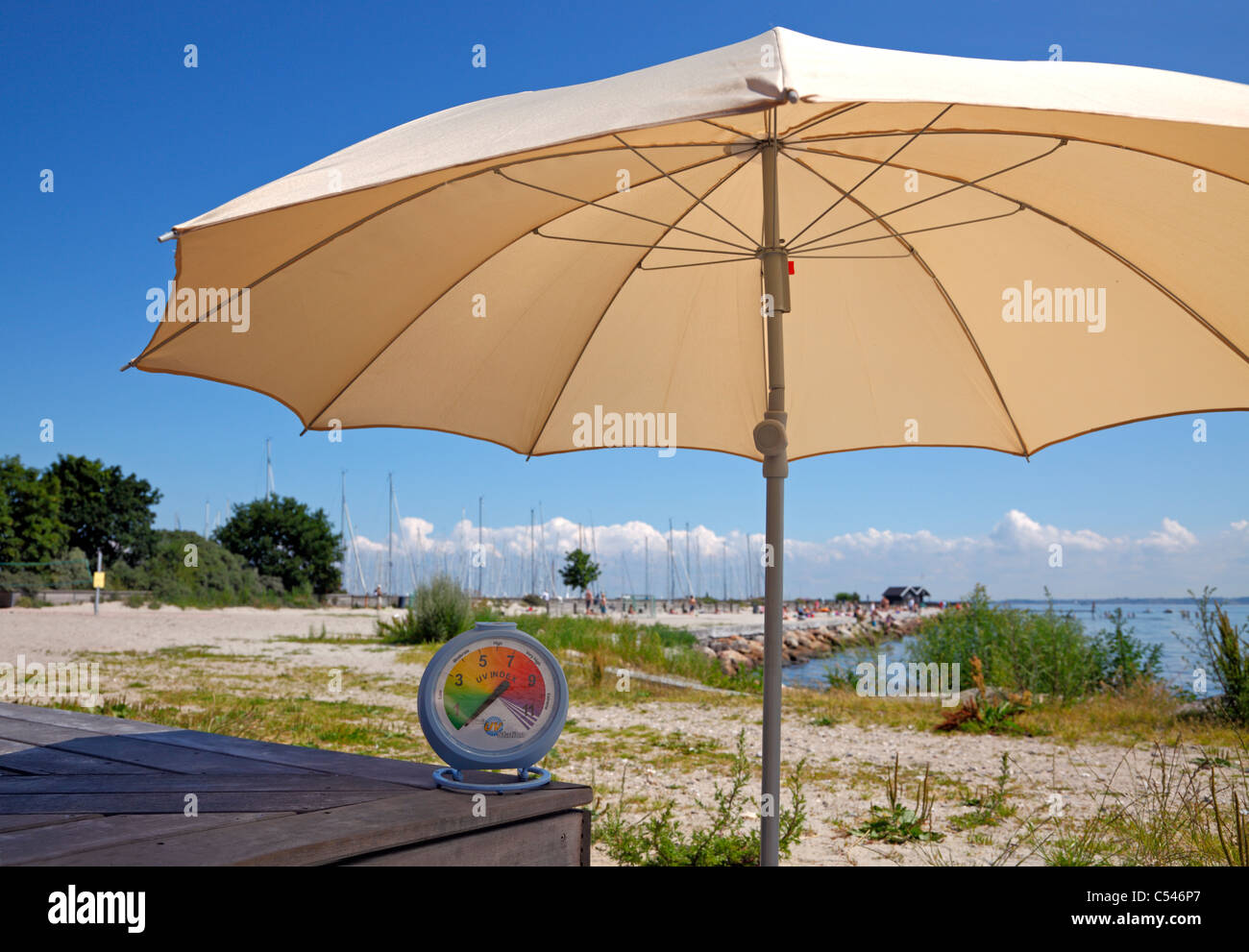 Una soleada tarde de julio en la playa. Un parasol hace la lectura del índice de UV en la estación sun UV portátil caer considerablemente Foto de stock