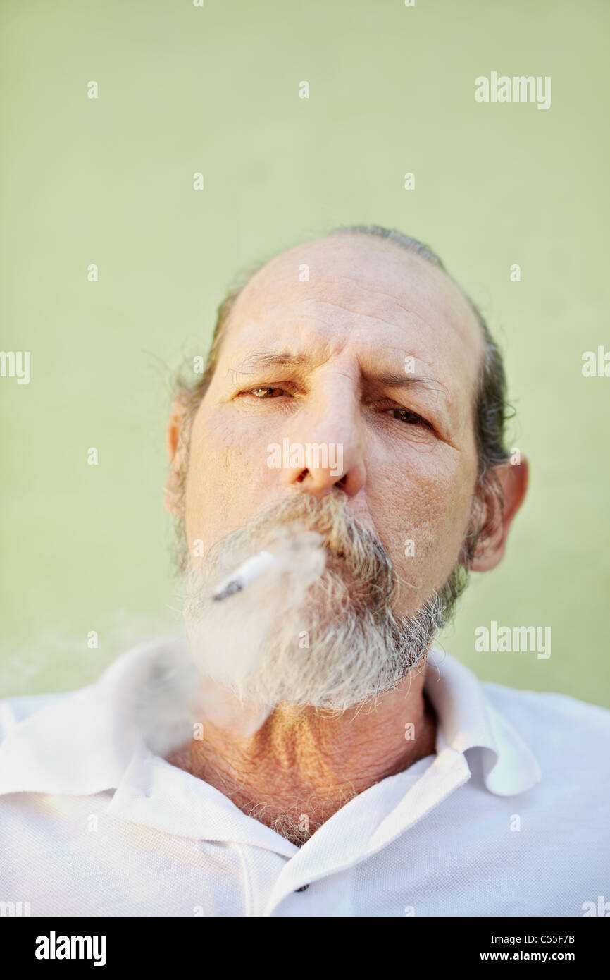 Retrato del hombre blanco maduro mirando a la cámara contra la pared verde con el cigarrillo en la boca. Espacio de copia Foto de stock