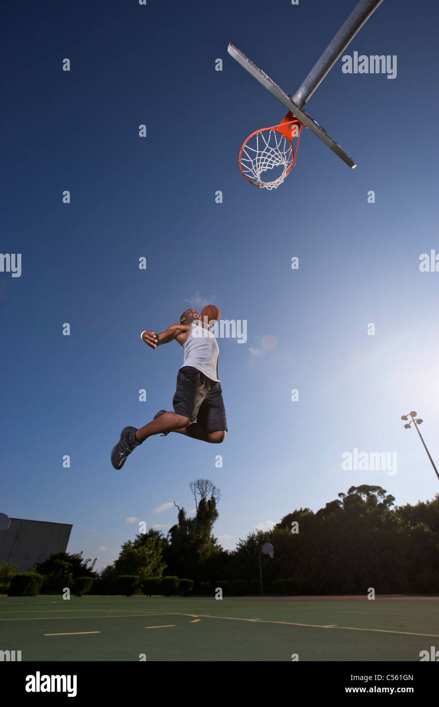 Macho haciendo slam dunk durante el juego de baloncesto al aire libre Foto de stock