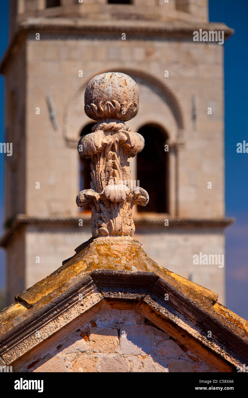 Finial tallados en piedra en el tejado con el campanario de la iglesia más allá en el casco antiguo de Dubrovnik, Dalmacia Croacia Foto de stock