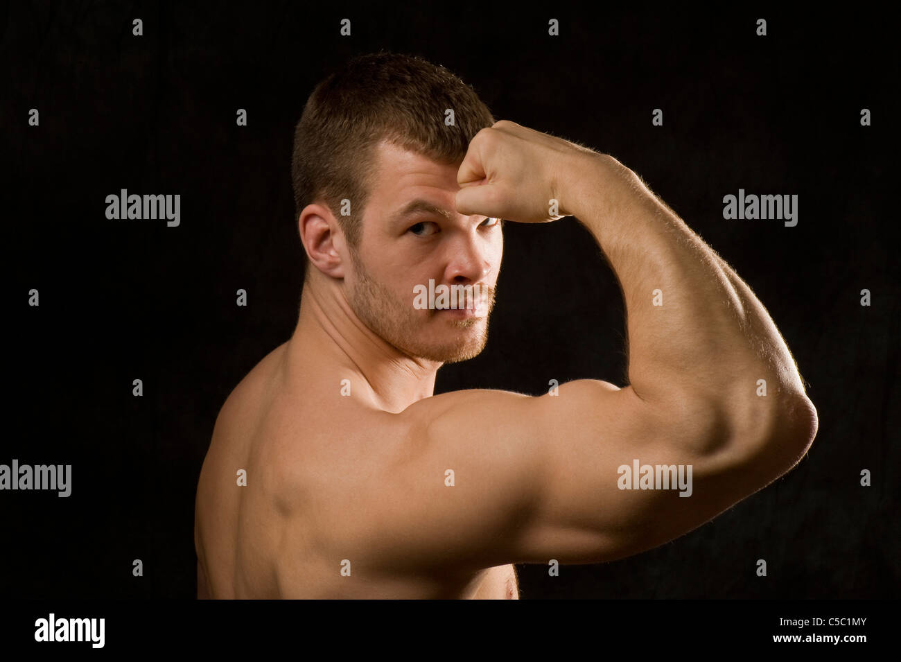 Close-up retrato de hombre macho flexionando los músculos sobre fondo negro Foto de stock