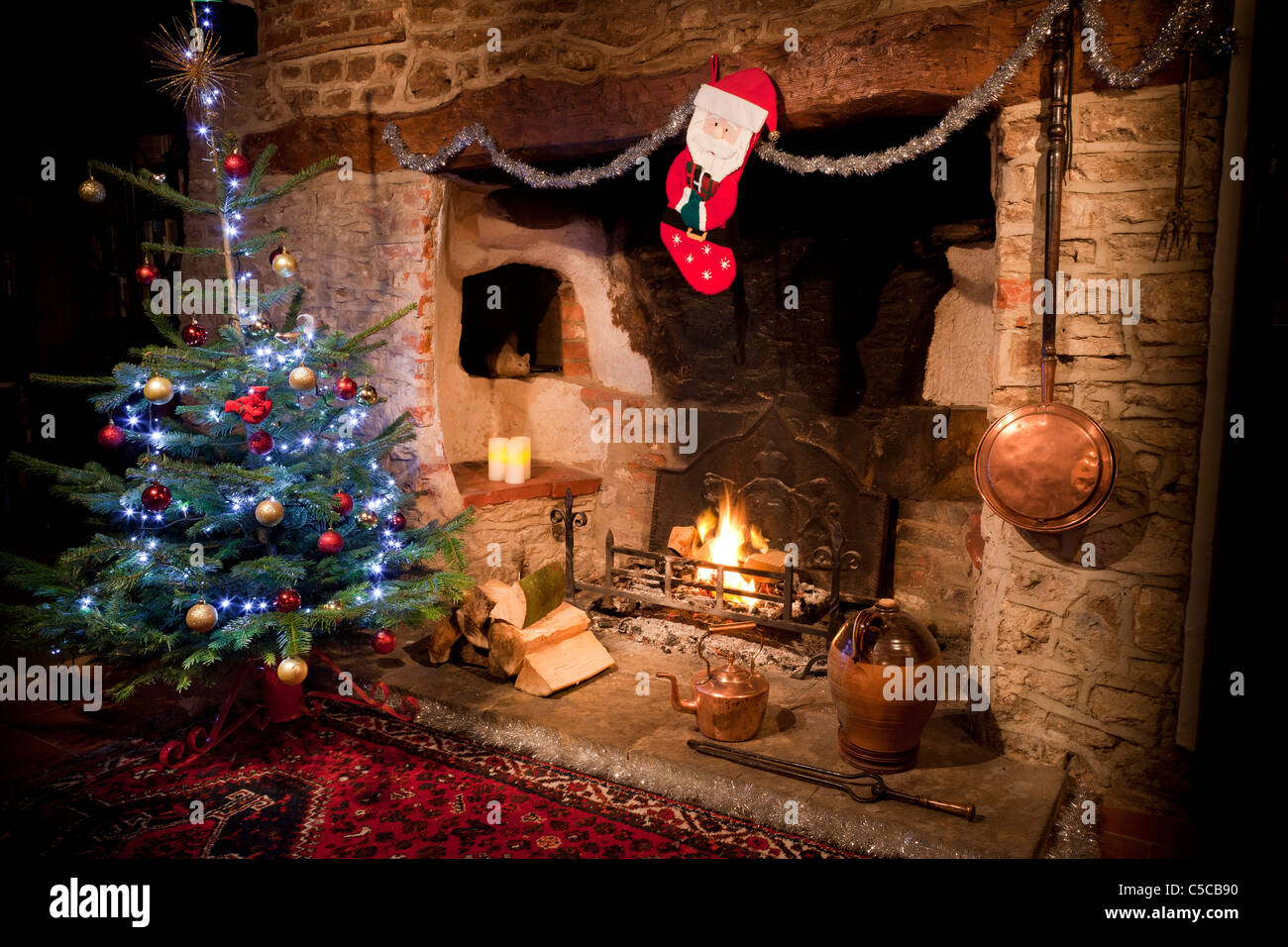 Chimenea en casa antigua con ardor bajo fuego de leña y el árbol de Navidad decorado, el almacenaje y la tetera de cobre. JMH5162 Foto de stock