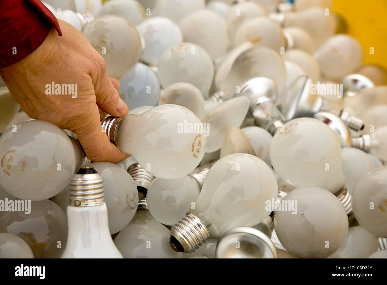 Close-up de una mano sujetando la bombilla entre muchas lámparas de reciclaje Foto de stock