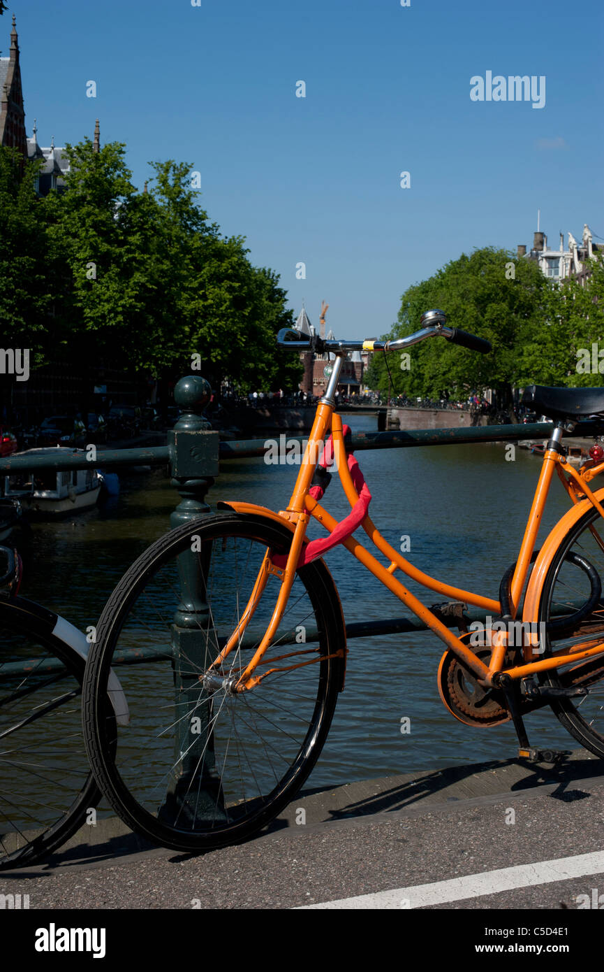 Bicicleta Naranja encadenado a un puente sobre un canal en Amsterdam Foto de stock