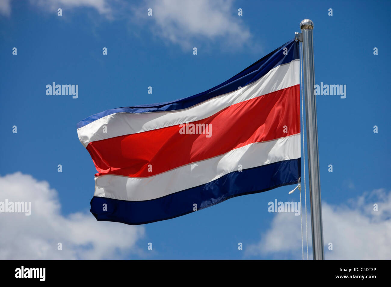 Ángulo de visión baja de Costa Rican bandera ondeando contra el cielo azul y las nubes Foto de stock
