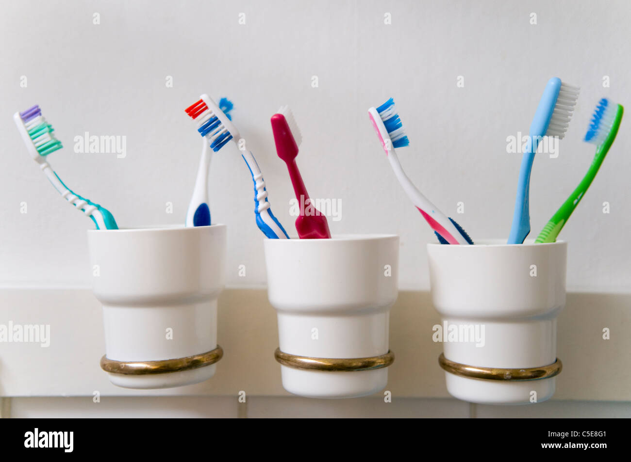Close-up de cepillos de dientes en tres soportes en fila contra la pared en el cuarto de baño Foto de stock