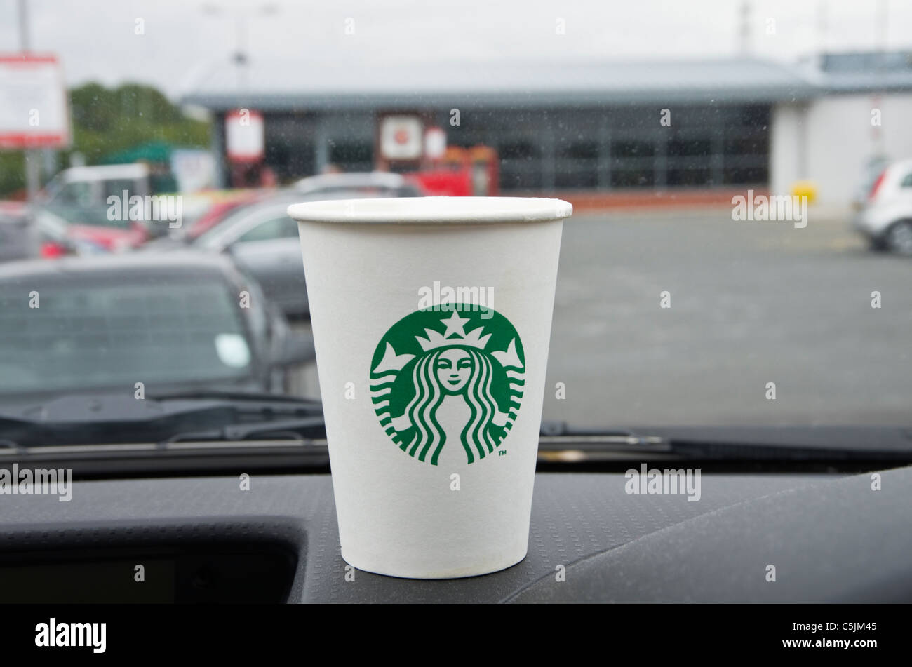 Starbucks café para llevar desechables para ir en un takeout vaso de papel para ir con el nuevo logotipo en el salpicadero de un coche en una estación de servicio de autopista. Inglaterra, Reino Unido. Foto de stock