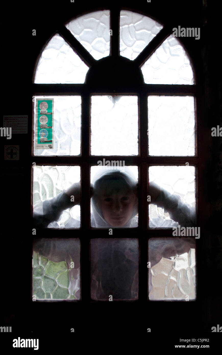 Un joven en una hoodie mirando a través del cristal de la puerta delantera. Foto de stock
