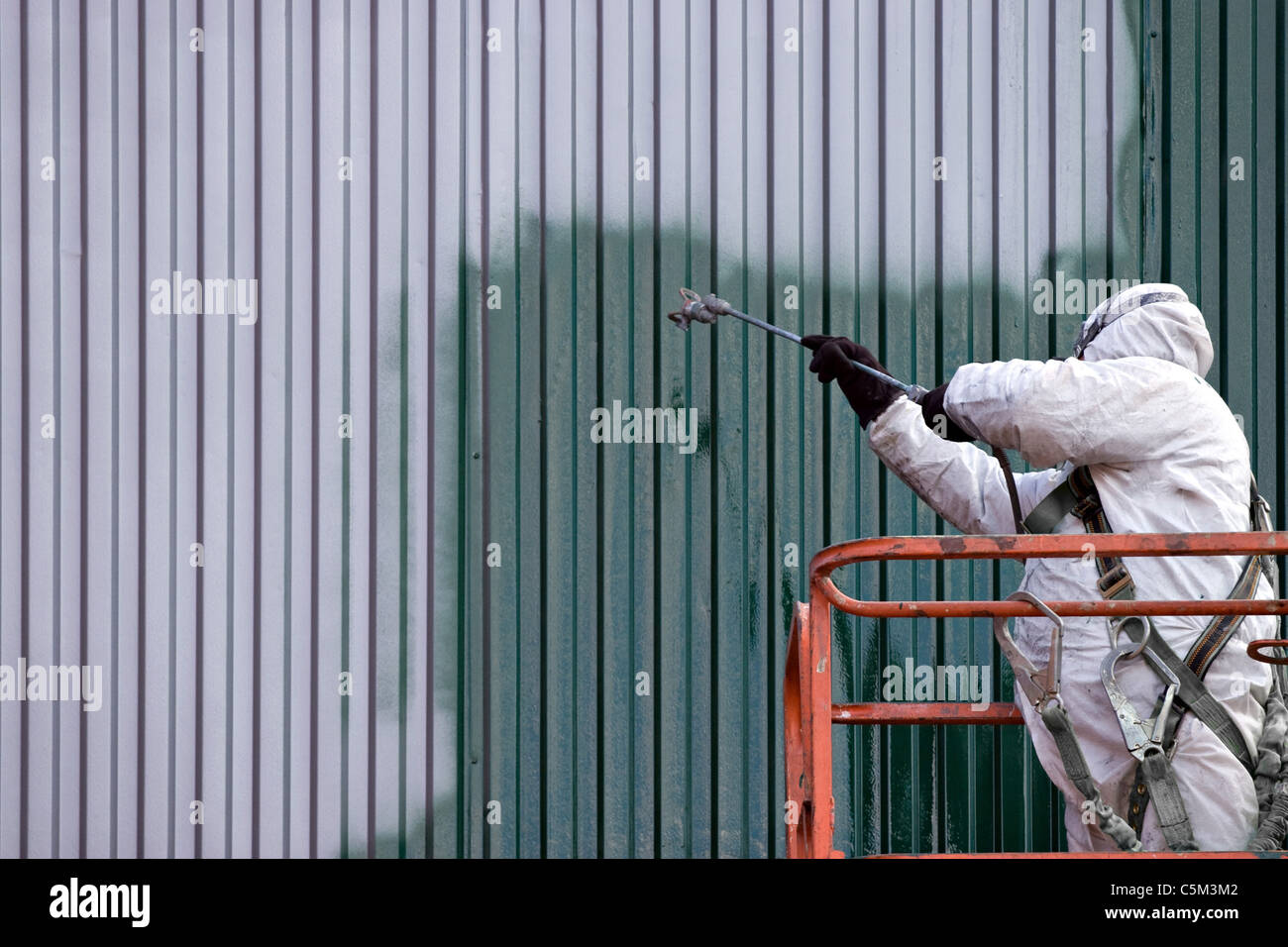 Un pintor comercial sobre una elevación industrial de pintura de pared exterior de acero o conducto. Foto de stock