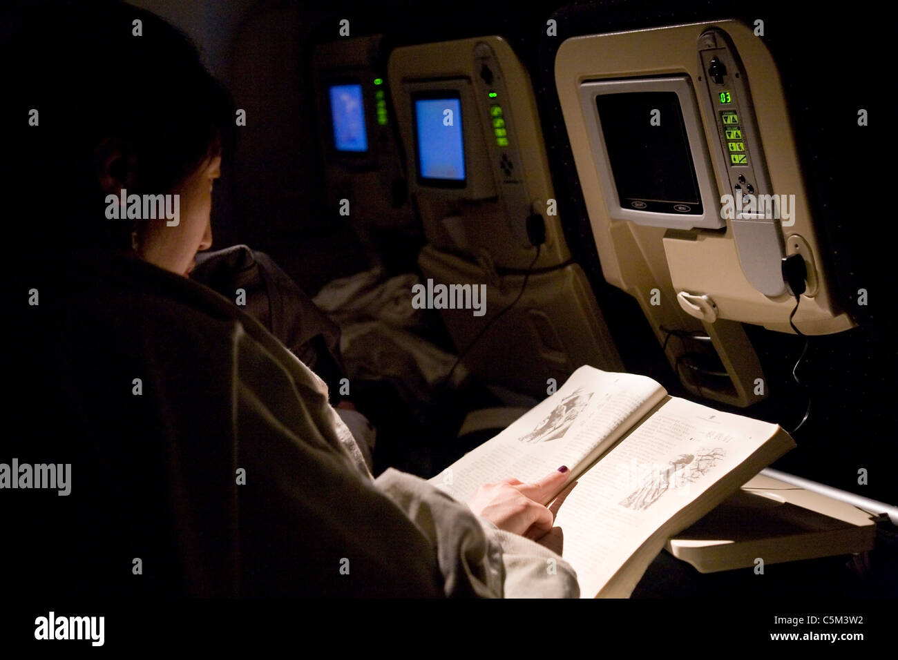 Mujer de pasajeros de aerolíneas / lectura lee un libro chino durante una larga distancia / distancia avión vuelo nocturno / avión / En avión. Foto de stock