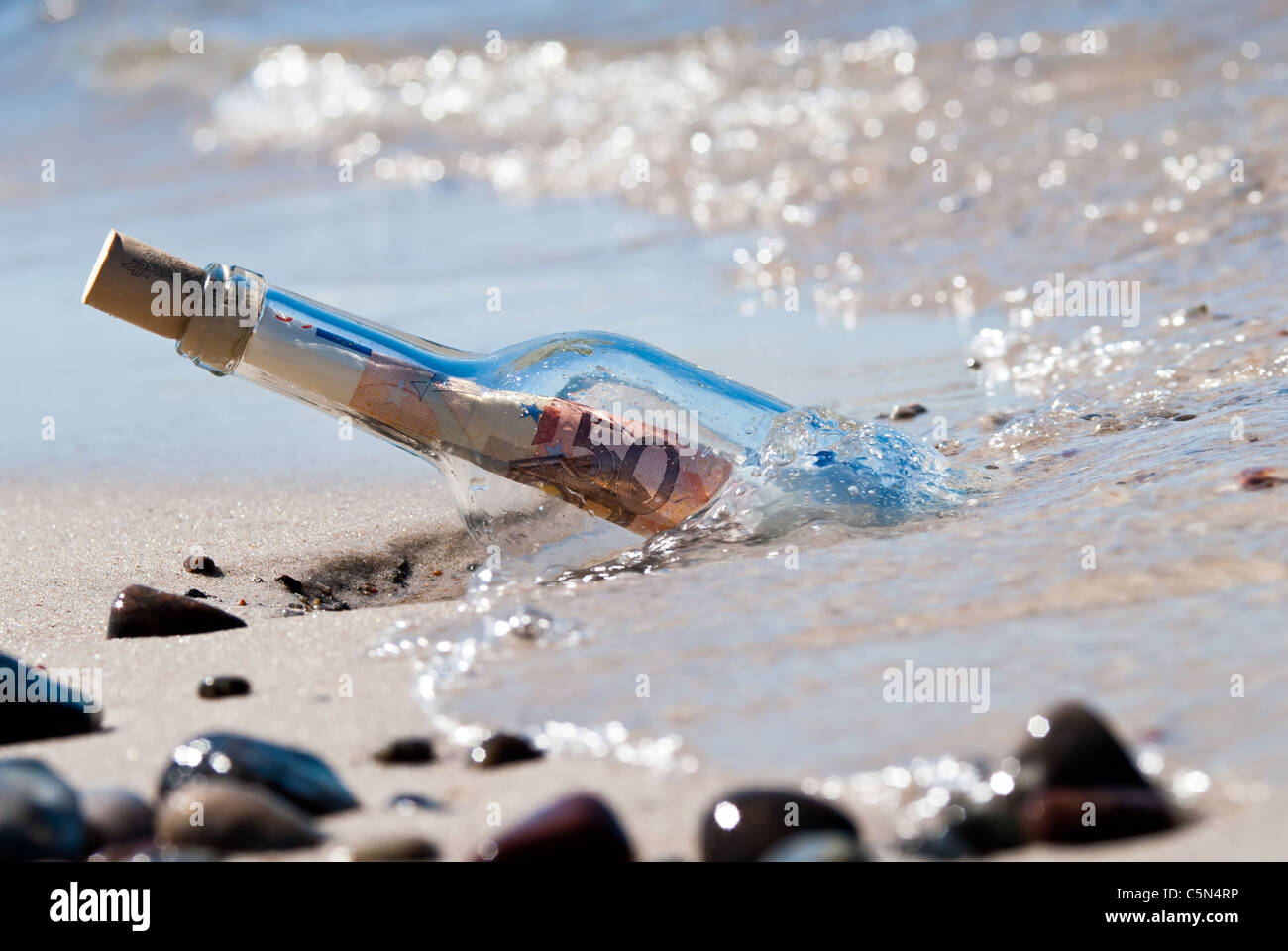 Un mensaje en una botella en la playa plenamente con euronotes Foto de stock