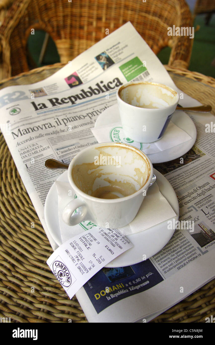 Tazas de café vacía con un recibo de 5.200 euros y un ejemplar del periódico "La Repubblica" en una cafetería en Italia Foto de stock