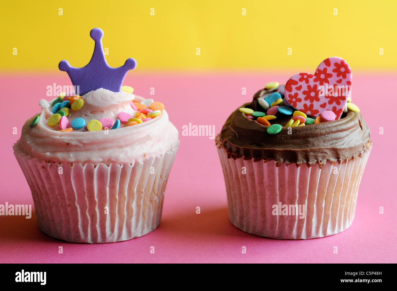 Cupcake de vainilla y chocolate con glaseado y espolvorea azúcar, corazón y corona Foto de stock