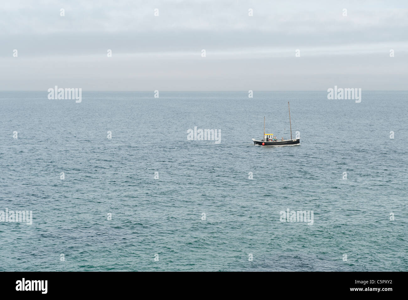 Un lejano barco de pesca frente a la costa de Cornwall velas silenciosamente sobre un mar en calma. Foto de stock
