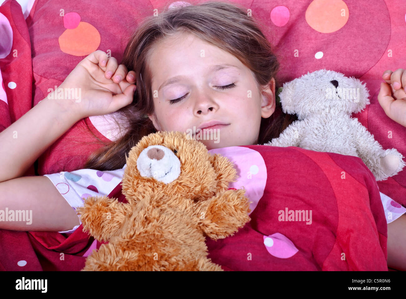 Una niña de ocho años de edad en la cama con mantas y almohadas y peluches Foto de stock