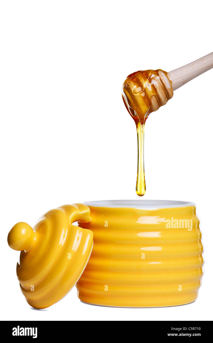 Foto de un bote de miel en forma de colmena amarilla con goteo penetrador celebrada anteriormente, aislado en un fondo blanco. Foto de stock