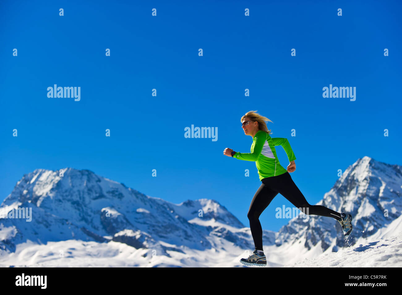 Una mujer correr rápido por montañas nevadas. Foto de stock