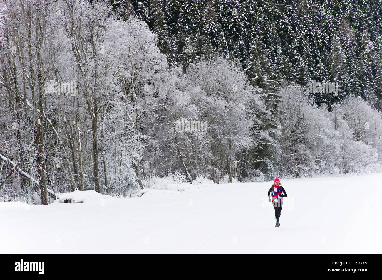 Un corredor corre sobre la nieve pasado campo nevado paisaje invernal. Foto de stock