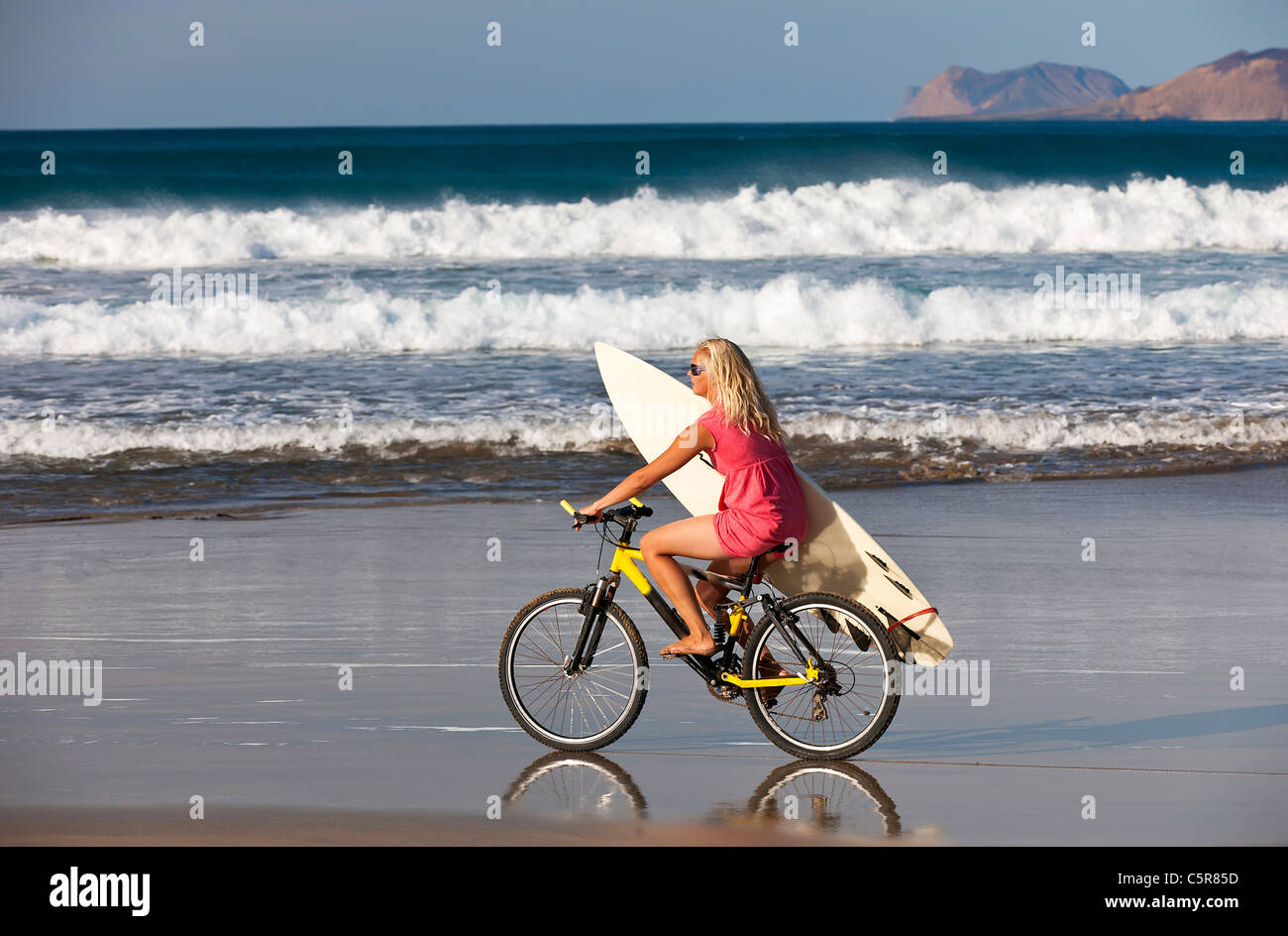 Surfer girl cabalga las olas del mar en bicicleta de montaña. Foto de stock