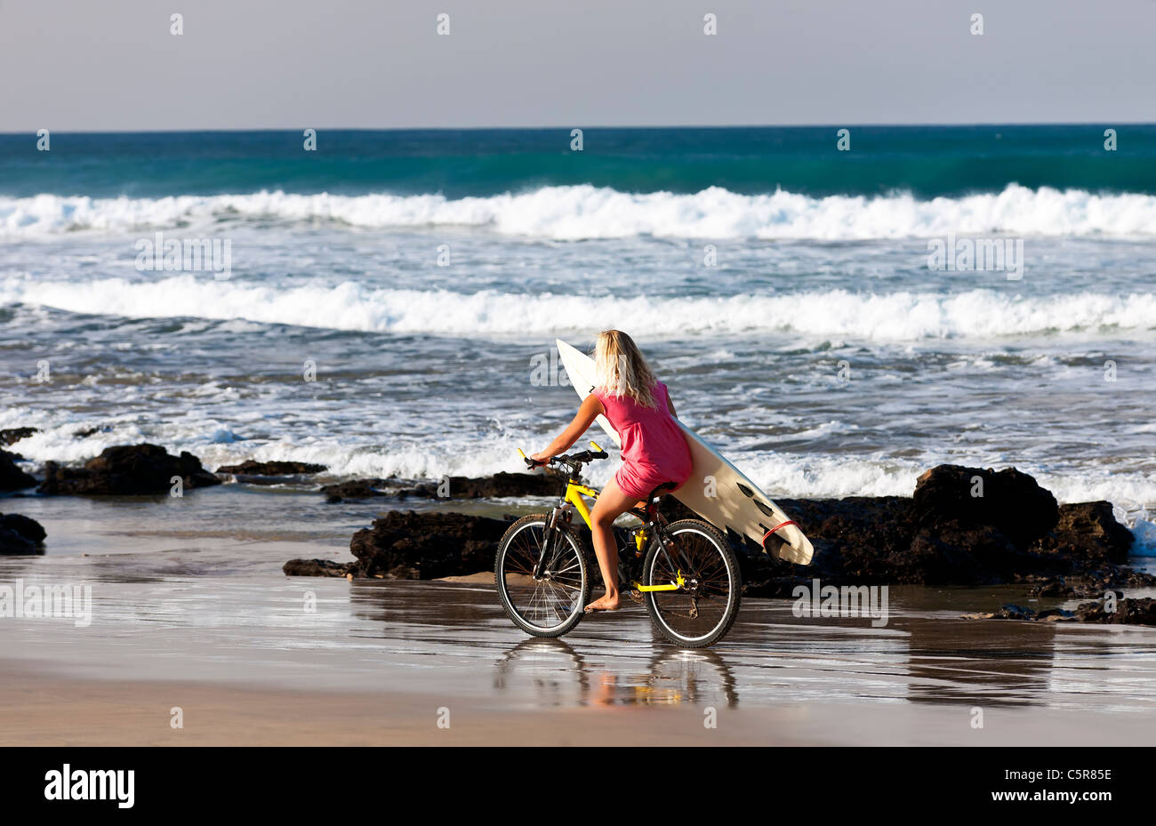 Una rubia surfer girl paseos por la playa con las olas. Foto de stock