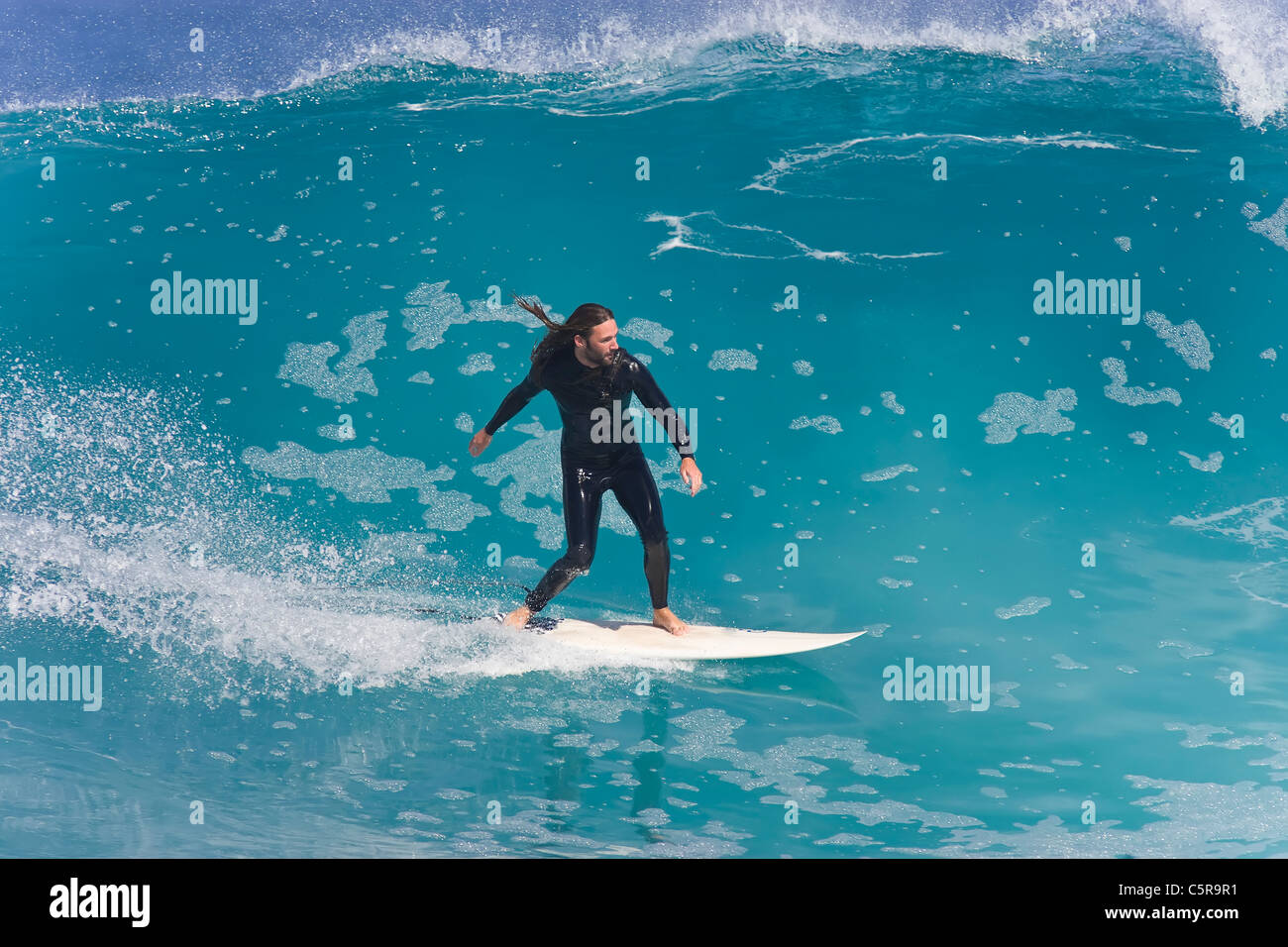 Surfer sonríe como él monta hermosa onda azul celeste. Foto de stock