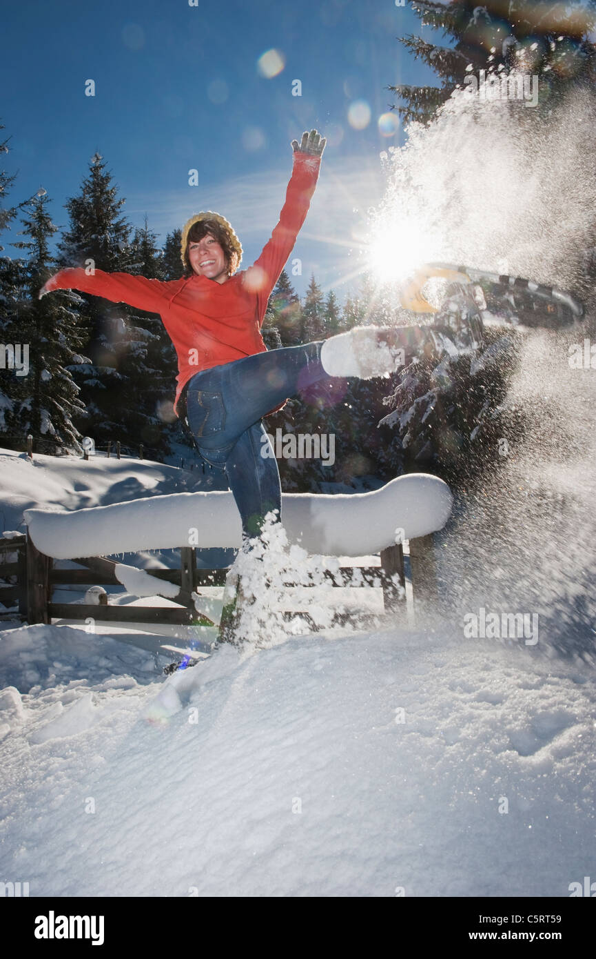 País Austria, Salzburgo, Flachau, joven mujer vistiendo zapatos de nieve saltando en la nieve Foto de stock