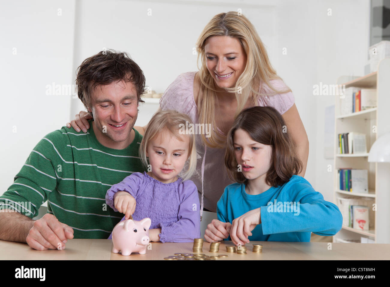 Alemania, Baviera, Munich, Familia con monedas y hucha, sonriendo Foto de stock