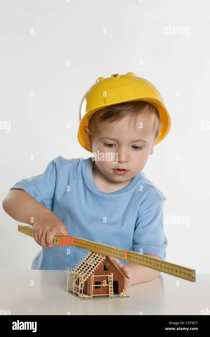Boy (2-3) vistiendo sombrero duro, jugando con la regla plegable Foto de stock