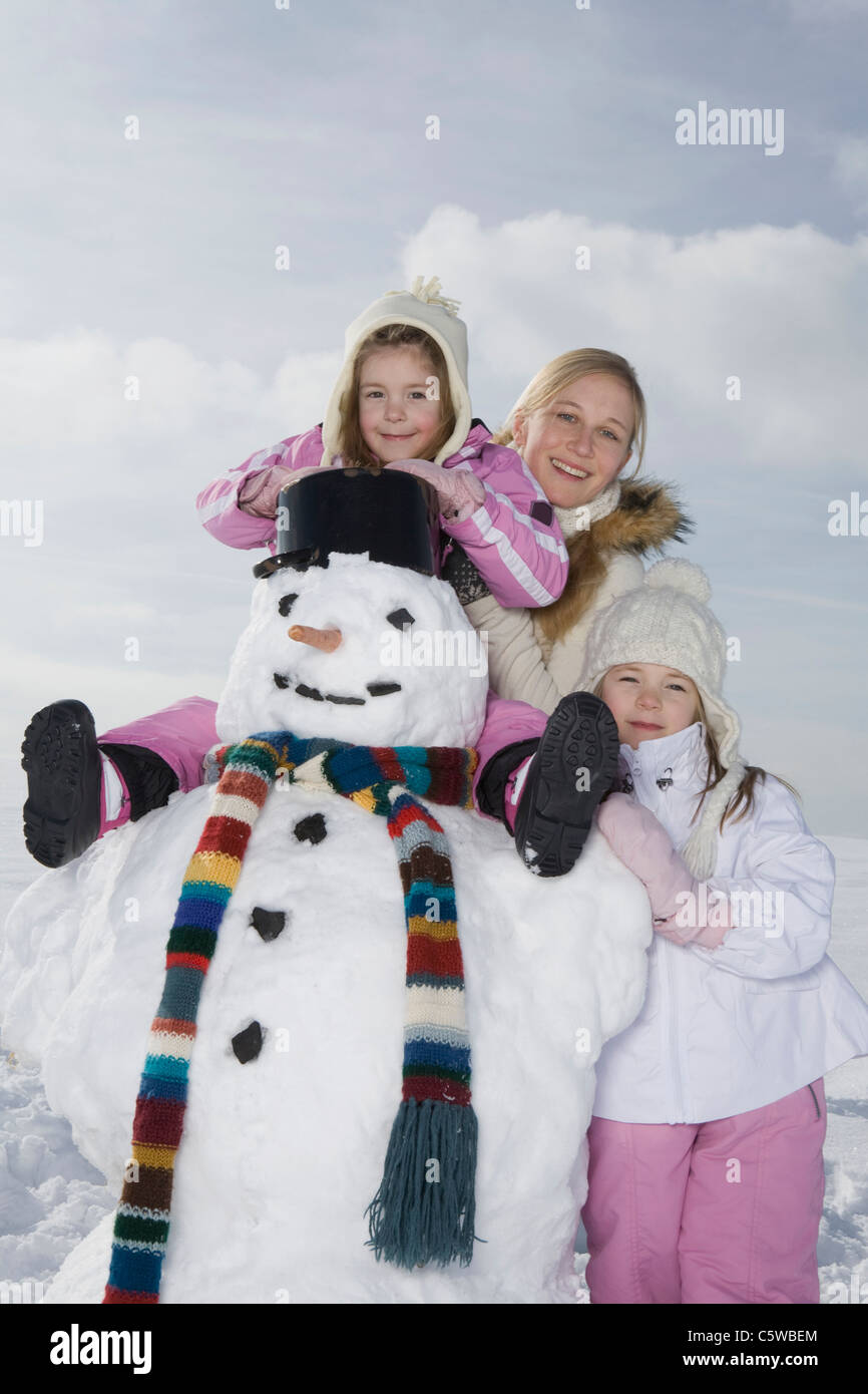 Alemania, Baviera, Munich, madre y sus hijas (4-5) (8-9) de pie junto al muñeco de nieve, sonriente, Retrato Foto de stock