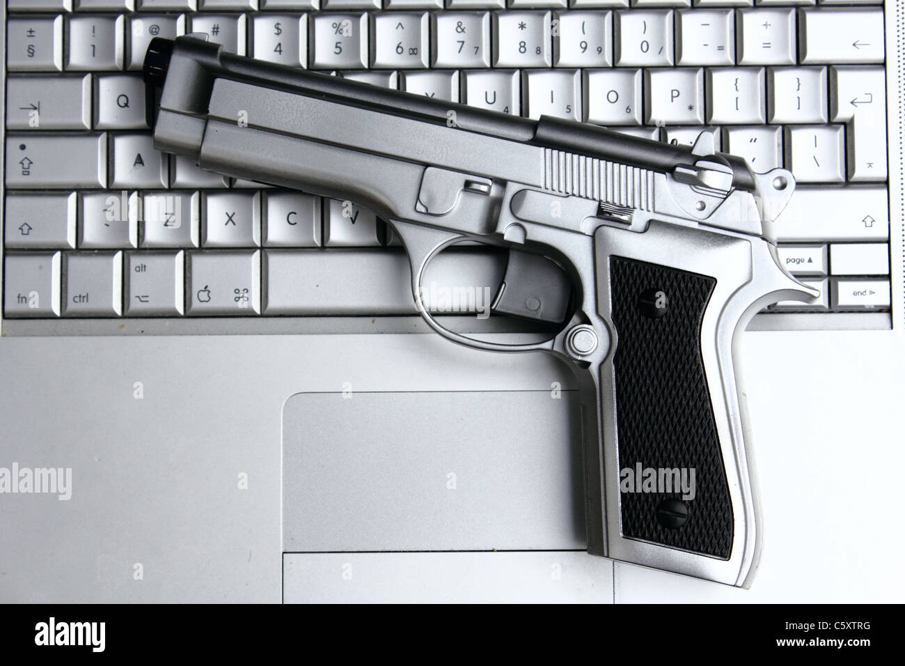 Una pistola de plata en un macbook pro , imagen conceptual , metáfora Foto de stock
