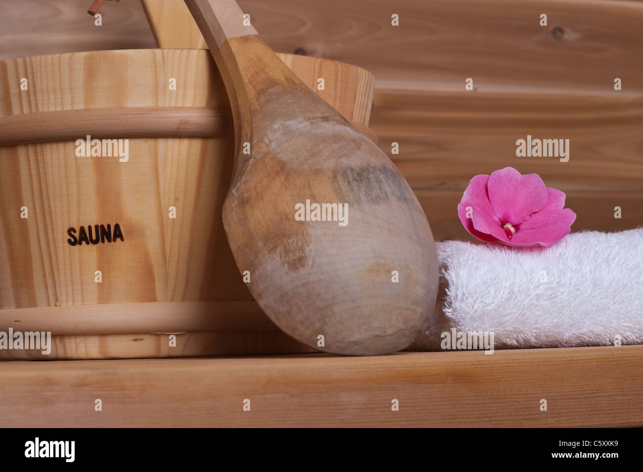 Toalla blanca con flor en la parte superior junto al cucharón con cucharón en una sauna de madera Foto de stock
