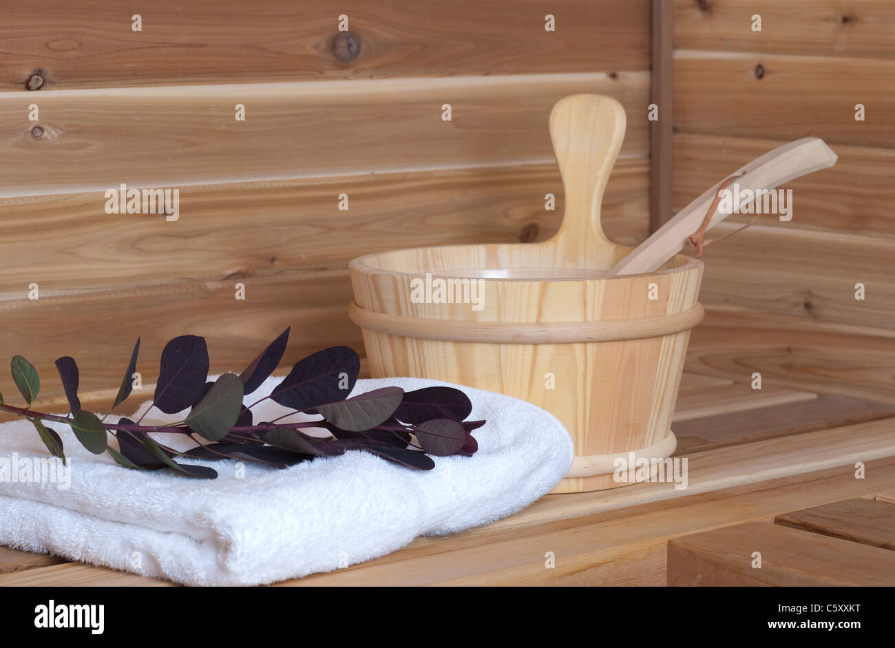 Sauna de madera con cuchara y cucharón junto a la toalla y flor Foto de stock
