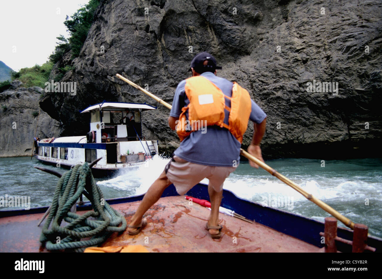 Barquero con un largo palo de bambú guías tour en barco Yangtze, afluente del río Daning Foto de stock