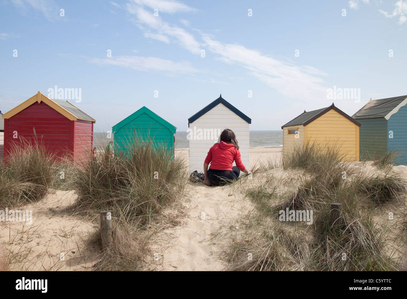 Una muchacha sentada delante de la playa, cabañas de playa Southwold, en Suffolk, Inglaterra. Foto de stock