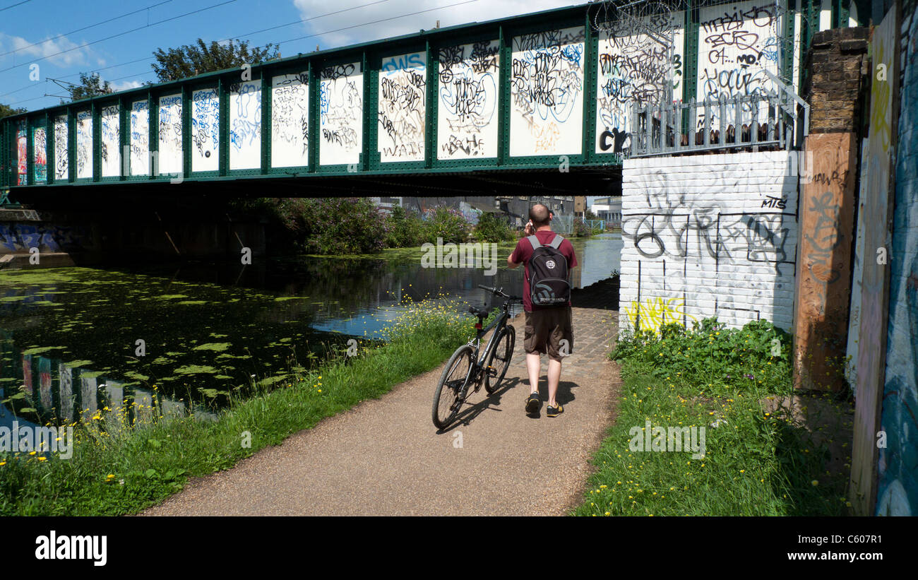 Un hombre con su bicicleta hablando por un teléfono móvil y caminando bajo un puente en el valle de Lea a pie Lee la navegación río East London UK KATHY DEWITT Foto de stock