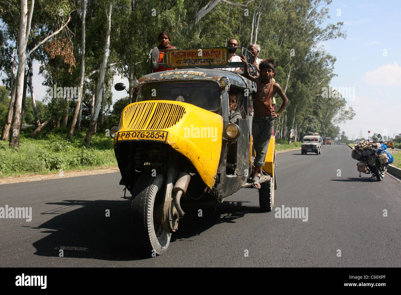 Los pasajeros se aferran al techo de una concurrida vintage tres wheeler Bajaj Tempo taxi bus en la campiña de Punjab del norte de la India Foto de stock