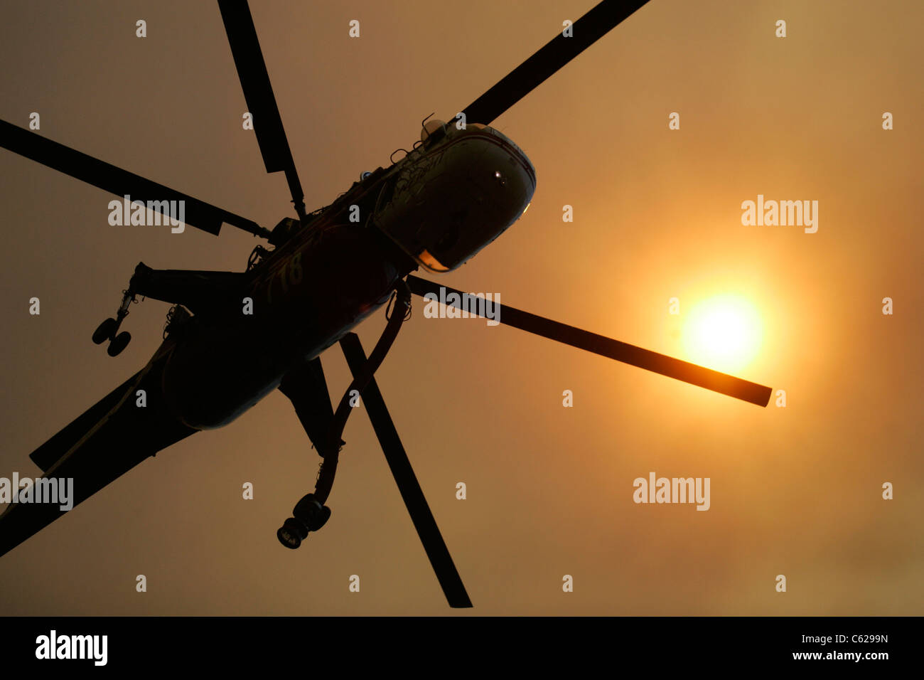 Un agua helicóptero vuela bajo un hijo carmesí filtrada por el humo de un incendio Foto de stock