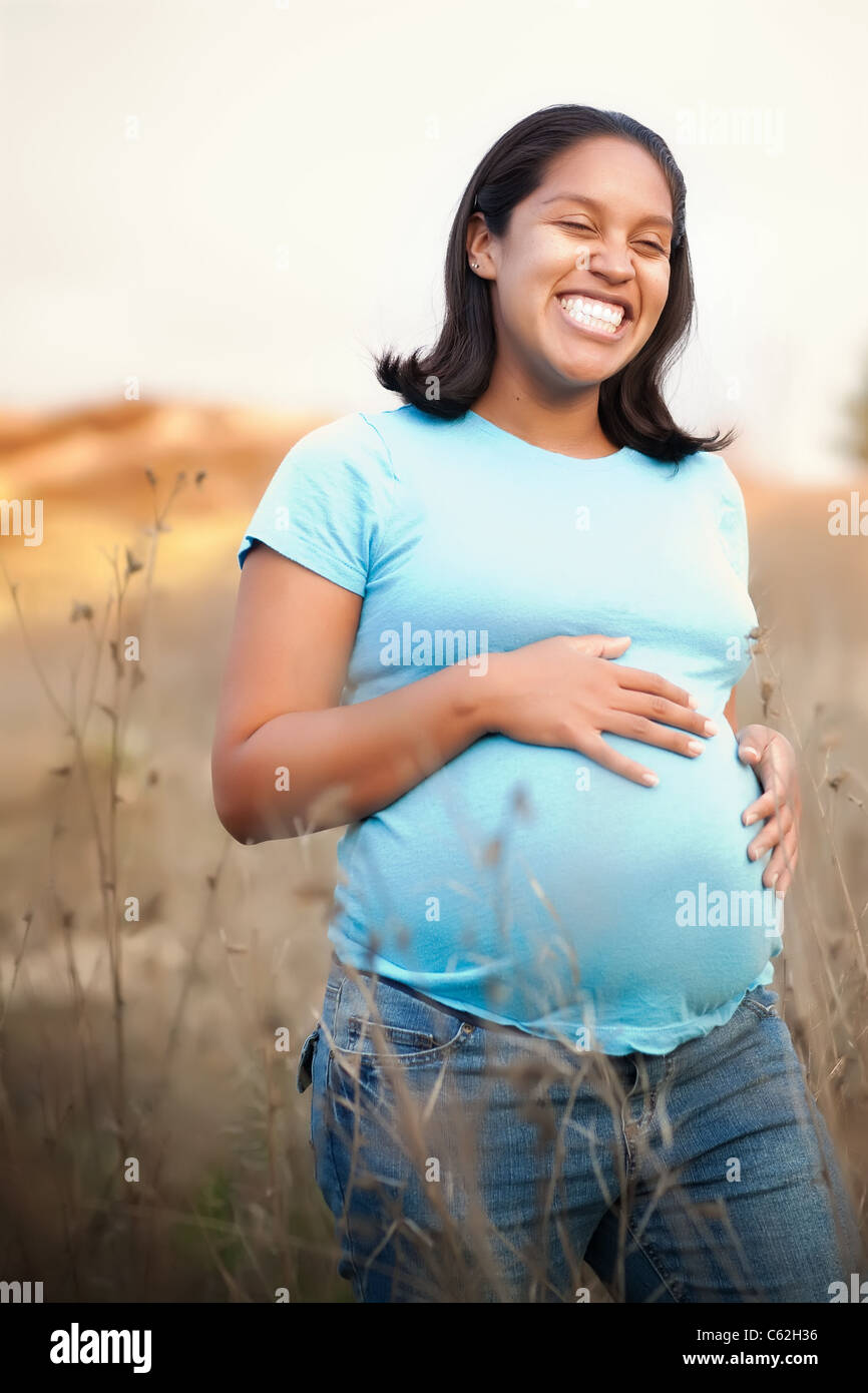 Sonriente joven mexicana embarazada sosteniendo su vientre y expresando su  alegría por el bebé que está llevando al caminar al aire libre en  California Hills Fotografía de stock - Alamy