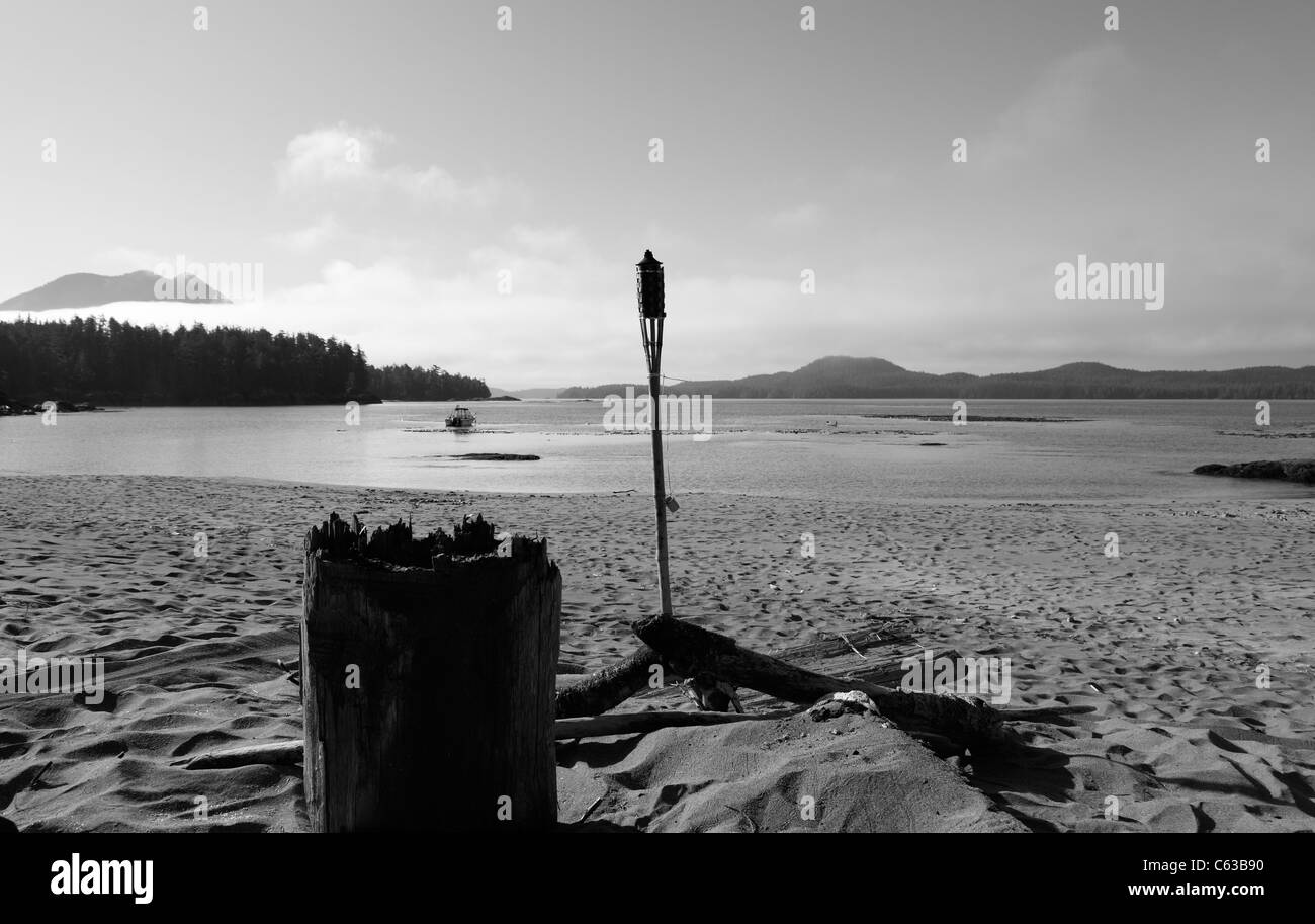 Registro y tiki antorcha alrededor de una fogata en una playa de arena en un día de verano cerca de Tofino BC Canadá Foto de stock