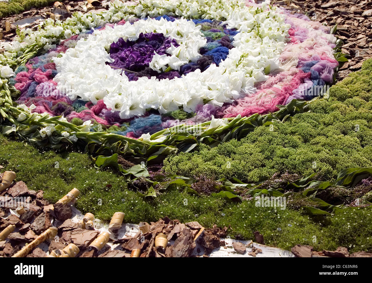 Bonito remolino está hecha de blanco y flores violetas con plantas verdes alrededor Foto de stock