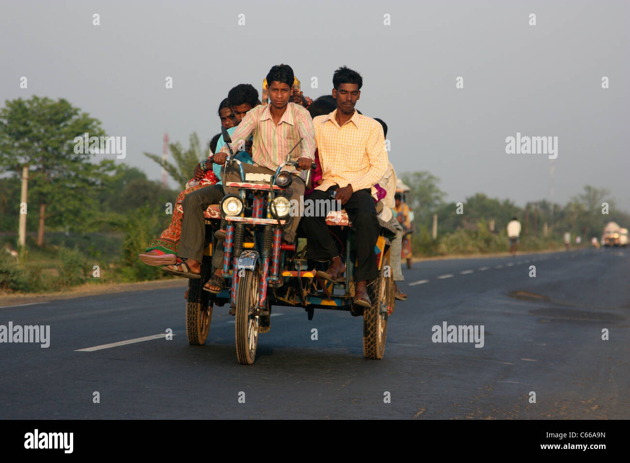 Indios muy cargado triciclo rickshaw motor transportando pasajeros hasta una carretera al atardecer en Bengala Occidental, India Foto de stock