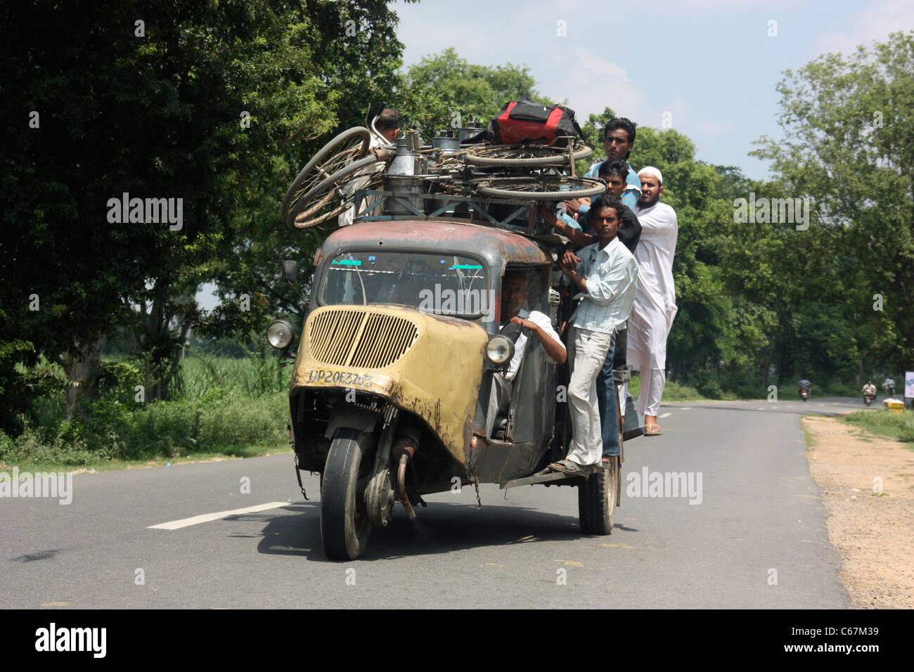 Los pasajeros se aferran al techo de una concurrida vintage tres wheeler Bajaj Tempo taxi bus en la campiña de Punjab del norte de la India Foto de stock