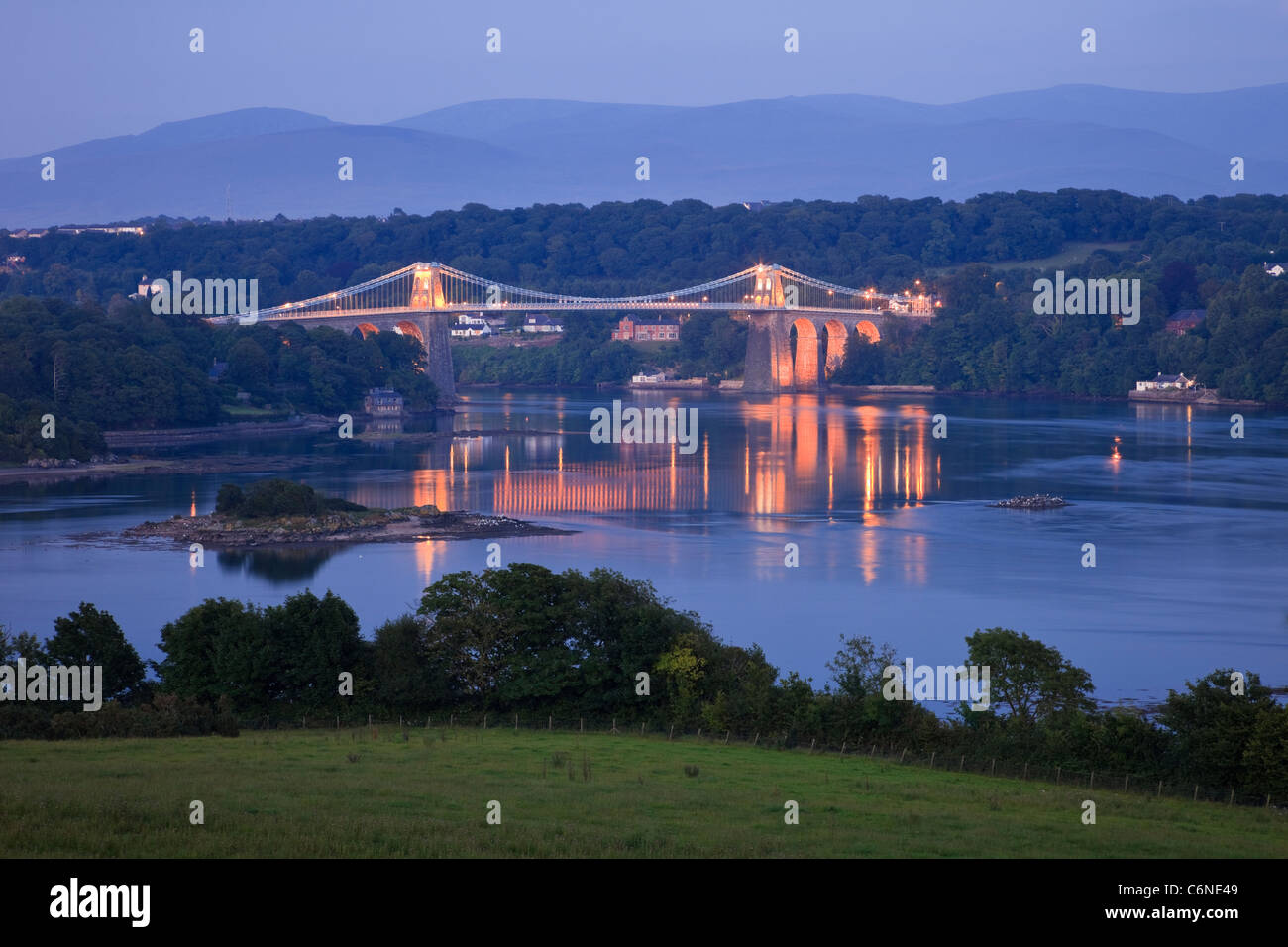 Vista del estrecho de Menai con canchas de Thomas Telford del puente colgante de Menai iluminados durante la noche. Menai Bridge, Isla de Anglesey, al norte de Gales, Reino Unido Foto de stock